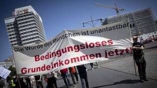 Demonstranten halten am 1. Mai 2024 in Berlin eine Transparent mit der Forderung nach einem   Bedingungsloses Grundeinkommen hoch