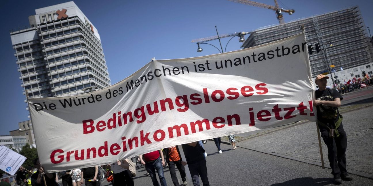 Demonstranten halten am 1. Mai 2024 in Berlin eine Transparent mit der Forderung nach einem   Bedingungsloses Grundeinkommen hoch