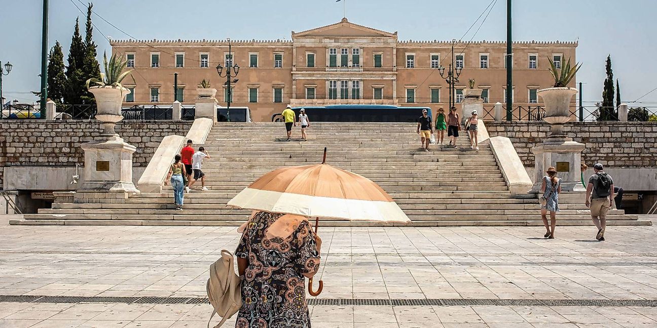 Eine Frau schützt sich mit einem Sonnenschirm  auf dem Syntagma-Platz in Athen vor der Sonne.